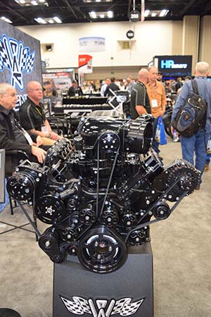 Engine with numerous belts and pulleys on stand with men on left sitting and three men standing on right