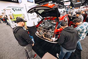 Three men looking at engine with Lamborghini valve covers installed in back of red SUV