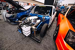 Engine installed in white race truck with blue Cadillac on left and orange Cadillac on right