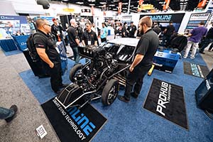 Men in trade show booth standing next to white car with exposed engine and large supercharger