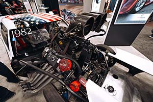 Race engine with large blower and Zoomie headers in white car with American flag on roof