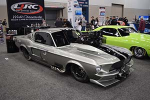 Silver Mustang with black racing stripes and large supercharger with lime green Dodge in background