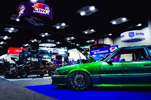 Green Ford Mustang with hood open and brown race car in background on left