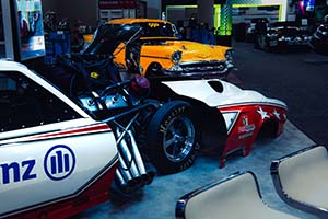 Red and white race car with engine exposed and front cover pulled back with yellow classic Chevrolet in background