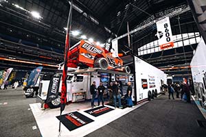 Orange modified race car with 15 on side sitting on ramp in white trailer