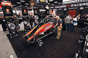 Man looking at orange and black sprint car body without wheels