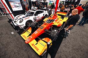 Red and yellow Indy car with DHL logos and white Porsche with two helmets on roof