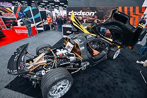 Black race car with gullwing doors open above car and engine exposed in back