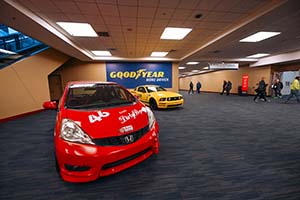 Red Honda Fit with yellow Ford Mustang in background