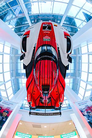 Red and white race car hanging from roof with glass ceiling behind it